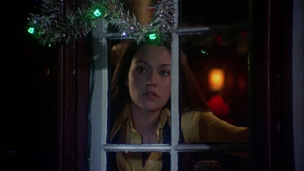 Die Hauptfigur aus 'Black Christmas' (1974), verkörpert von Olivia Hussey, blickt angstvoll aus dem Fenster – eine Szene, die die beklemmende Spannung und den klassischen Horror des Films einfängt.
