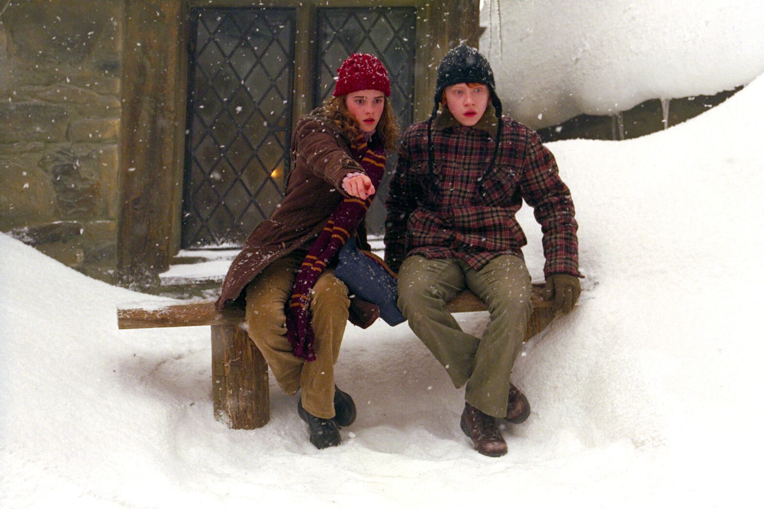 Ron Weasley und Hermine Granger, gespielt von Rupert Grint und Emma Watson, in einer stimmungsvollen Szene in Hogsmeade, eingehüllt in eine malerische Schneelandschaft – ein Bild, das die gemütliche und zauberhafte Atmosphäre des Winters in der Harry Potter-Welt einfängt.